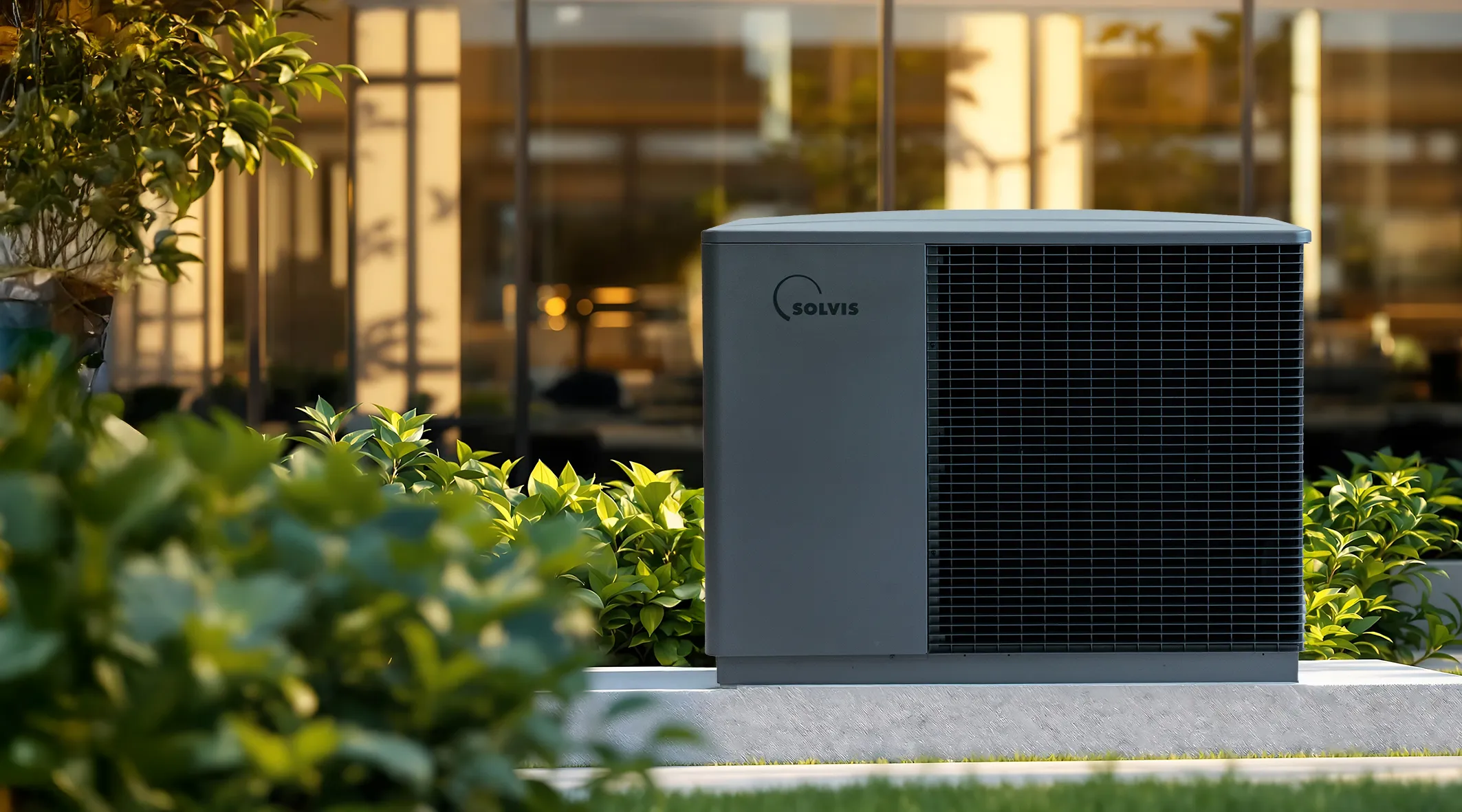 Eine Solvis-Wärmepumpe steht im begrünten Außenbereich vor einem modernen Gebäude, umgeben von Pflanzen und warmem Sonnenlicht.