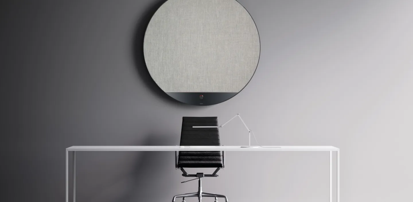 Ein minimalistischer Arbeitsplatz mit einem schlichten weißen Tisch, einem schwarzen Bürostuhl und einer modernen Schreibtischlampe. 