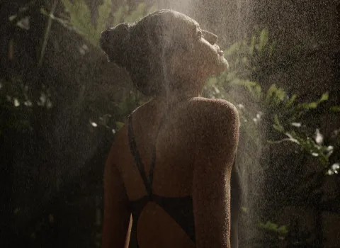 Frau steht unter der Dusche mit der Wassernebelfunktion der Serenity Sky von Dornbracht mit Pflanzen im Hintergrund.