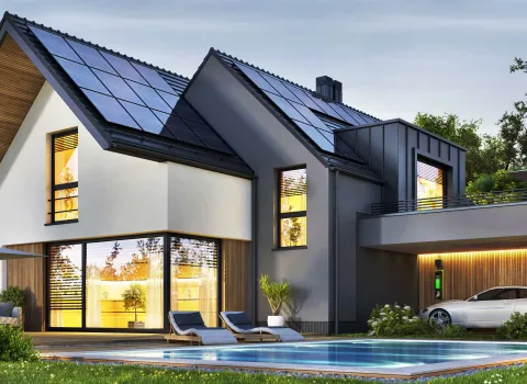 Nachtansicht eines schönen, modernen Hauses mit Sonnenkollektoren, Wallbox und Swimmingpool.