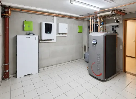 Ein **Solvis Energiesystem im Technikraum** mit großem Pufferspeicher, Batteriespeicher und mehreren wandmontierten Steuer- und Wechselrichterkomponenten. Kupferleitungen verbinden die einzelnen Anlagenteile zu einem kompakten Heizungs- und Energiesystem.