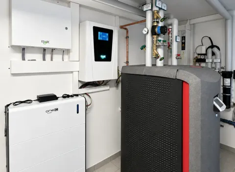 Ein moderner Technikraum zeigt eine Solvis Heizungsanlage mit großem, grau-schwarzem Speicher sowie mehreren elektronischen Komponenten an der Wand. Links sind weiße Steuerungs- und Speichermodule installiert, während isolierte Rohrleitungen, Ventile und Messinstrumente die Anlage verbinden. Die sauber ausgeführte Installation verdeutlicht eine kompakte Haustechniklösung für Heizung und Energiemanagement.