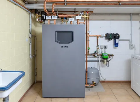Eine Solvis Heizungsanlage im Technikraum mit großem grauem Speichersystem, Kupferleitungen, Ausdehnungsgefäß und verschiedenen Armaturen. Die Anlage ist übersichtlich installiert und mit Filtern, Messgeräten sowie weiteren Komponenten der Heizungs- und Wassertechnik verbunden.