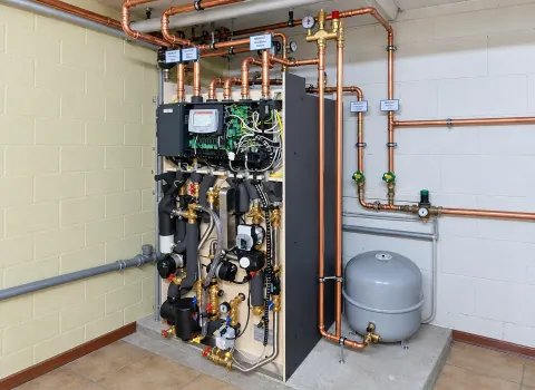Eine Solvis Heizungsanlage im Technikraum mit geöffneter Verkleidung zeigt die integrierte Regelungs- und Hydrauliktechnik. Sichtbar sind zahlreiche Kupferleitungen, Pumpen, Ventile, Sensoren, elektrische Komponenten sowie ein angeschlossenes Ausdehnungsgefäß.