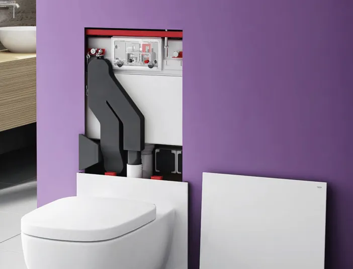 Eine wandhängende Toilette mit abgenommener Frontplatte zeigt die verborgene Installation des TECElux-Systems in einer lilafarbenen Wand. 